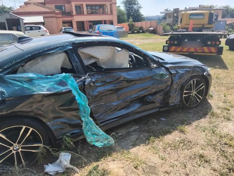 A grey BMW 4 Series with heavy damage down the driver's side, on the back of a tow truck yard
