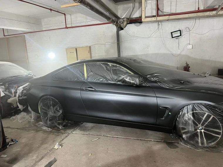 The same BMW in matte primer, masked in plastic inside the workshop